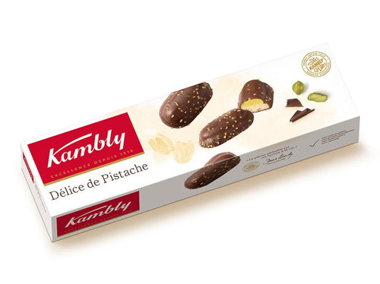 Kambly Délice de Pistache Kekse mit Pistazien, 90 g, auf einem weißen Teller mit Pistazien im Hintergrund