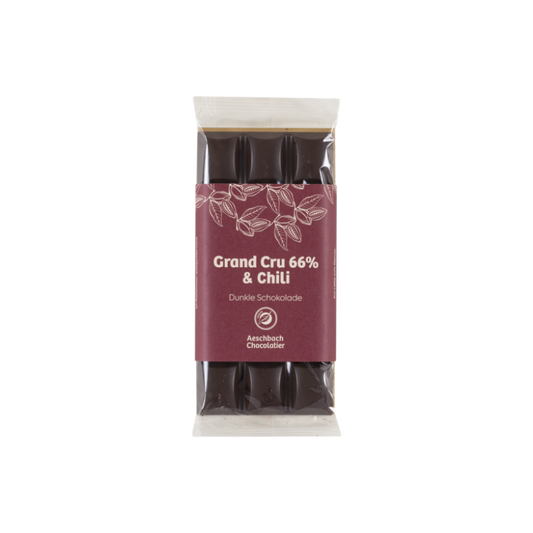 Dunkle Schokolade Grand Cru 66% mit Chiliflocken von Aeschbach Chocolatier, zeigt Stücke dunkler Schokolade mit Chiliflocken.